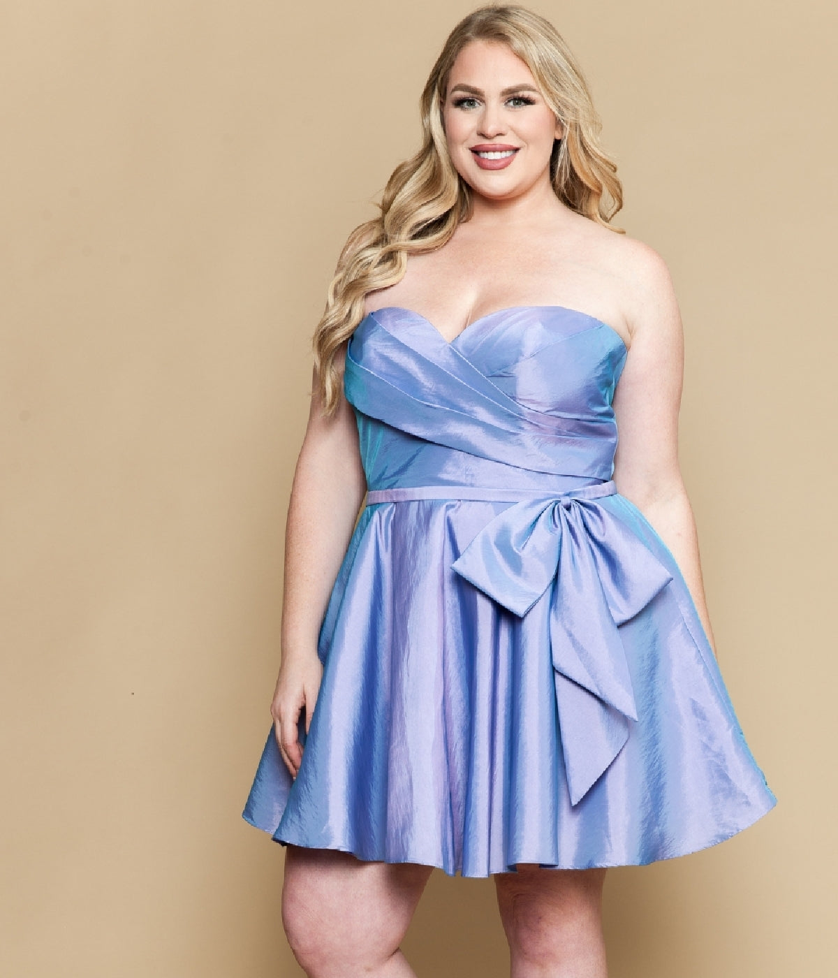 A woman models the Plus-Size Strapless Cocktail Dress: Poly USA W1214 in iridescent lavender with a large waist bow, standing against a beige background.